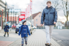 Kleiner Junge läuft neben Erwachsenem (Vater) auf Bürgersteig